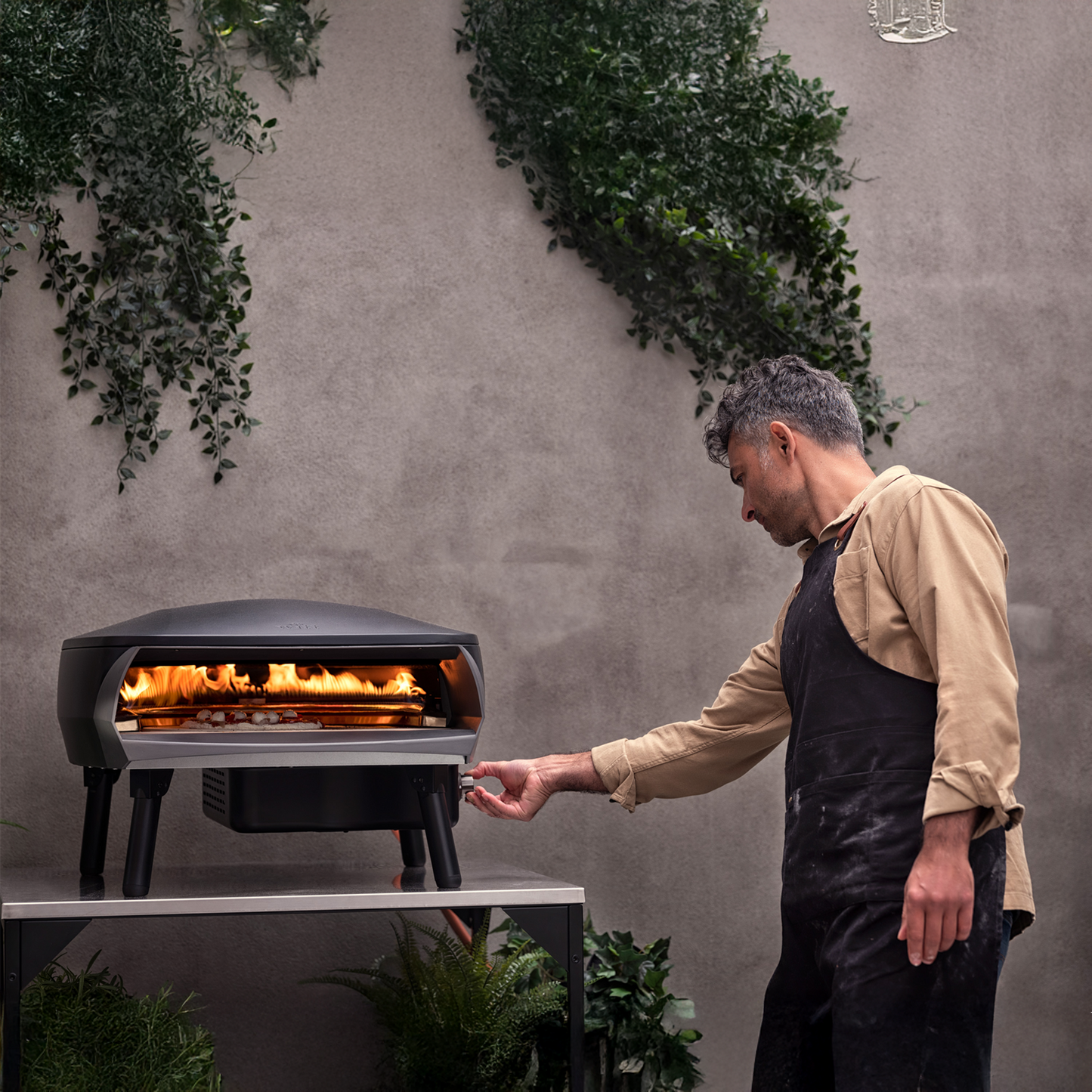 Man operating Witt Etna Rotante outdoor pizza oven with plants around