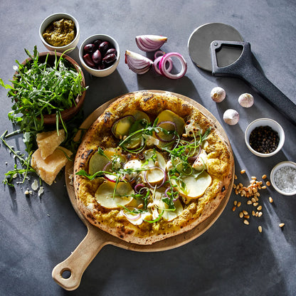 Vegetable pizza on a wooden board with ingredients and a Witt black pizza cutter on a dark surface