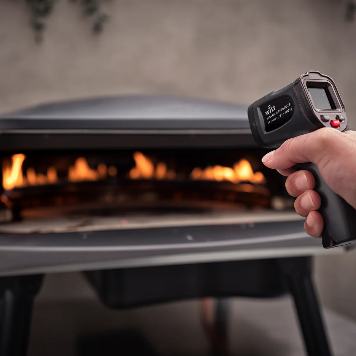 Person using a black Witt Pizza Infrared Temperature Gun to check the temperature of an open grill.